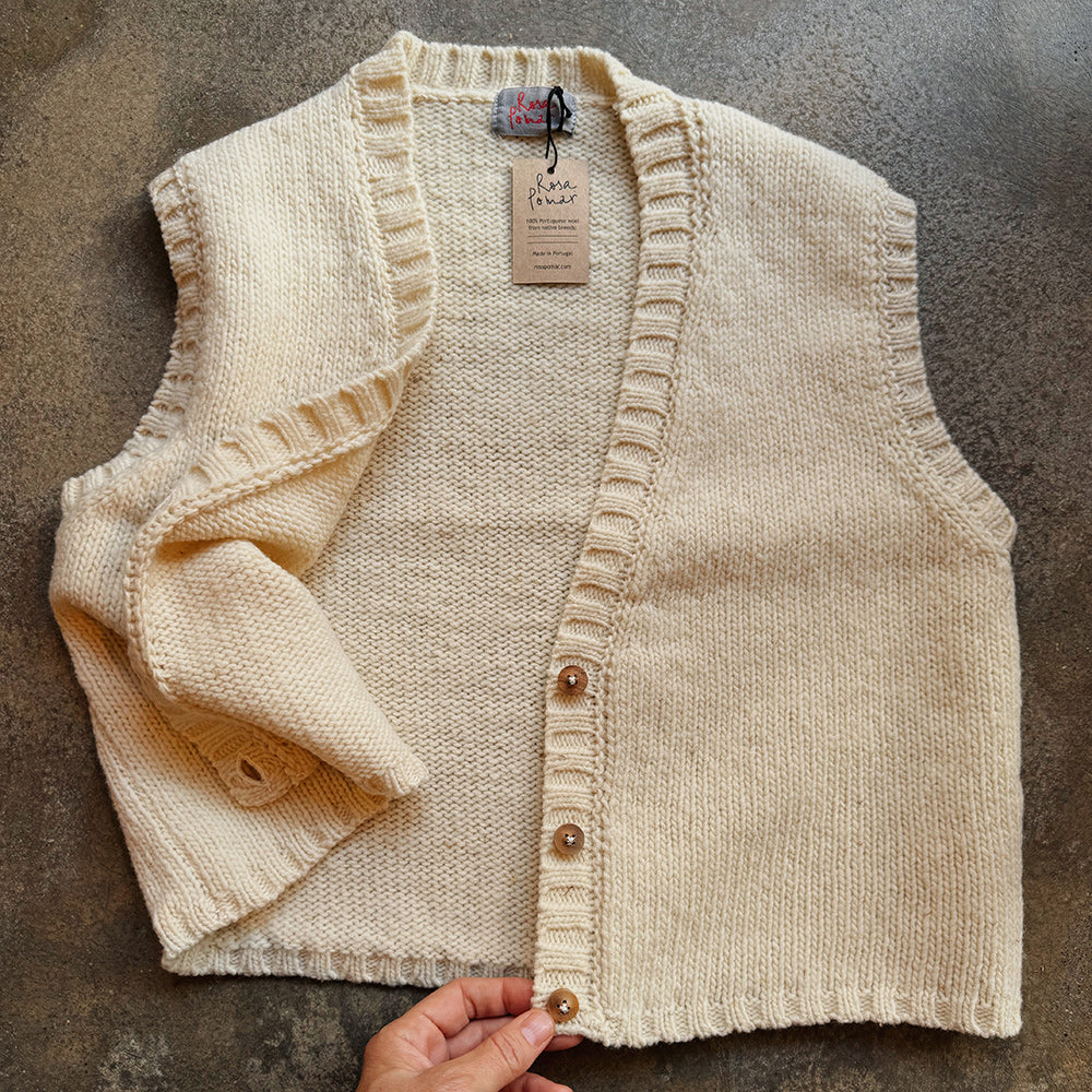 Beige knitted wool vest with buttons on a textured surface
