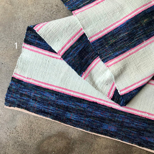 Handwoven rag rug with blue and pink stripes on a concrete surface