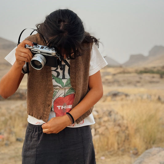 Person wearing a knitted wool vest, holding a camera in a desert landscape
