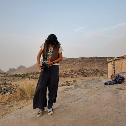 Person wearing a knitted wool vest, standing on a rocky outcrop with mountains and a clear sky in the background