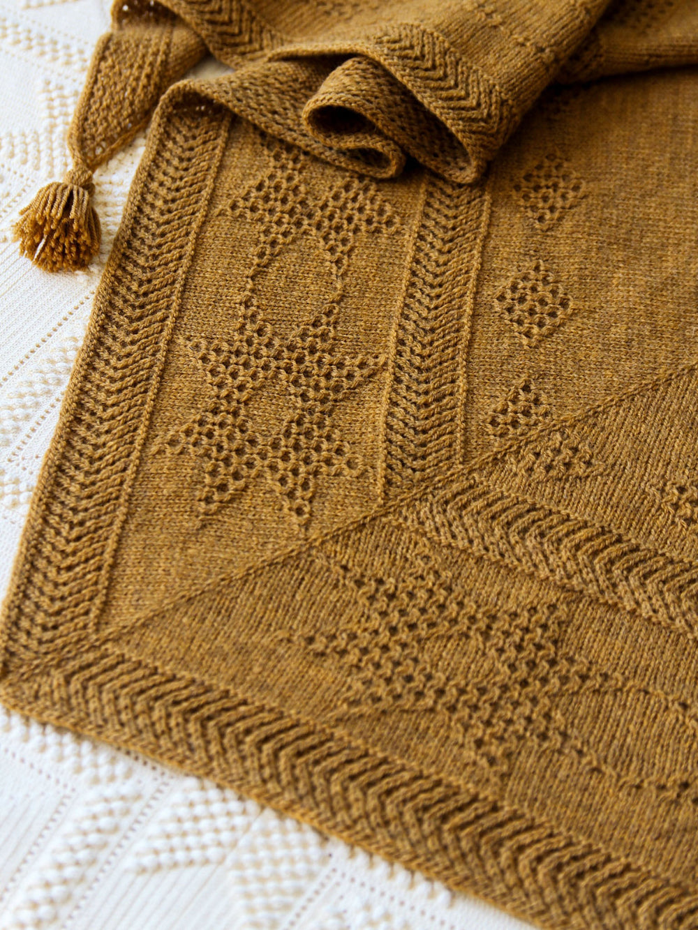 A close-up of the Oisin shawl in Mondim B580, featuring textured geometric patterns and a tassel detail.