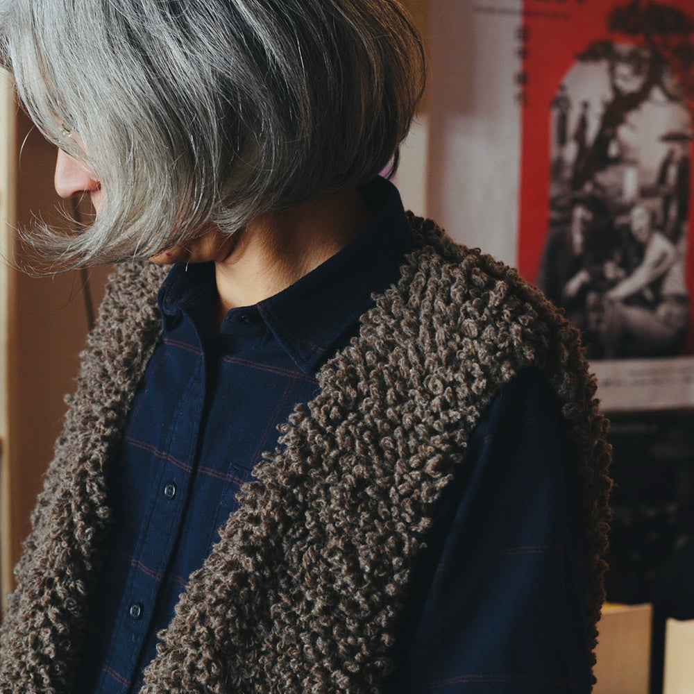 Person wearing a brown textured knitted wool vest over a blue shirt with a blurred background