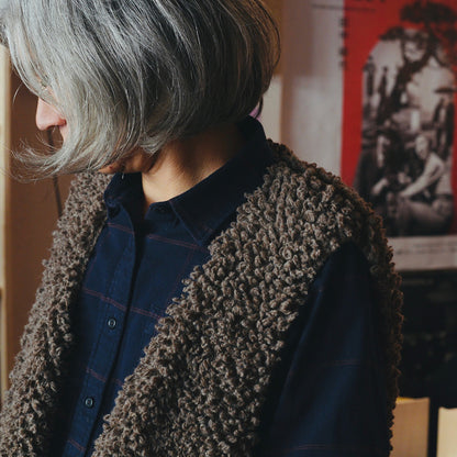 Person wearing a brown textured knitted wool vest over a blue shirt with a blurred background