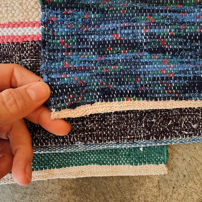 Close-up of a hand holding a piece of multicolored handwoven rag rug.