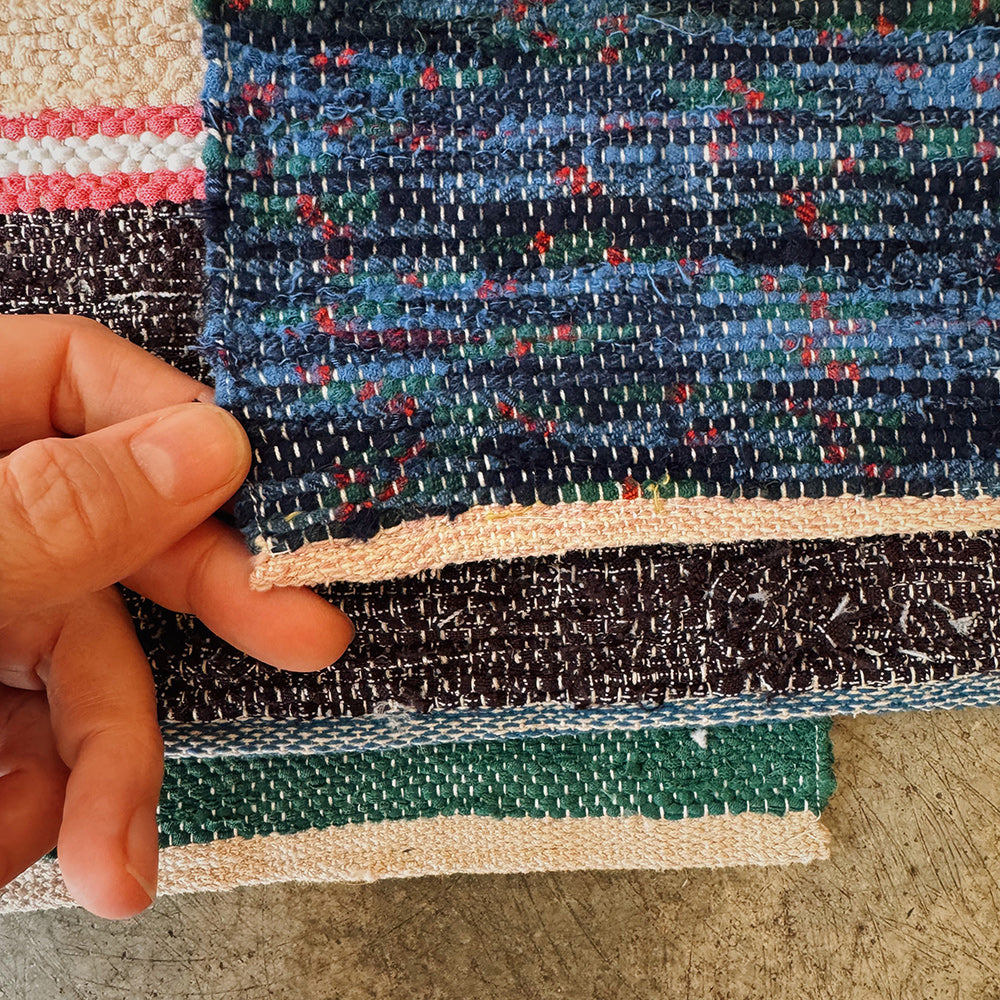 Close-up of a hand holding a piece of multicolored handwoven rag rug.