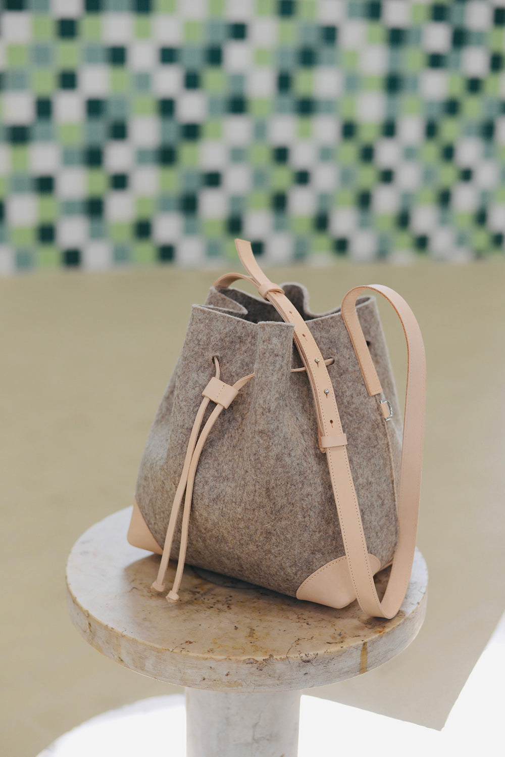 Brown felt bag with beige leather straps on a marble surface with a checkered wall background