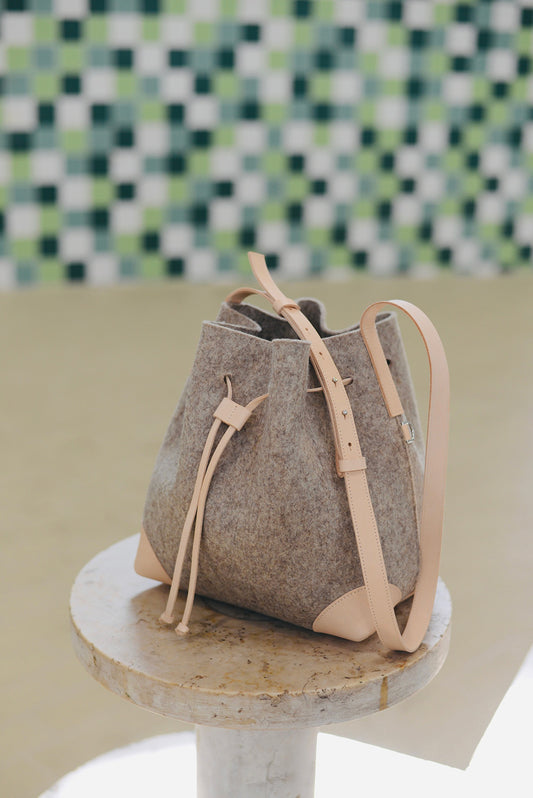 Brown felt bag with beige leather straps on a marble surface with a checkered wall background