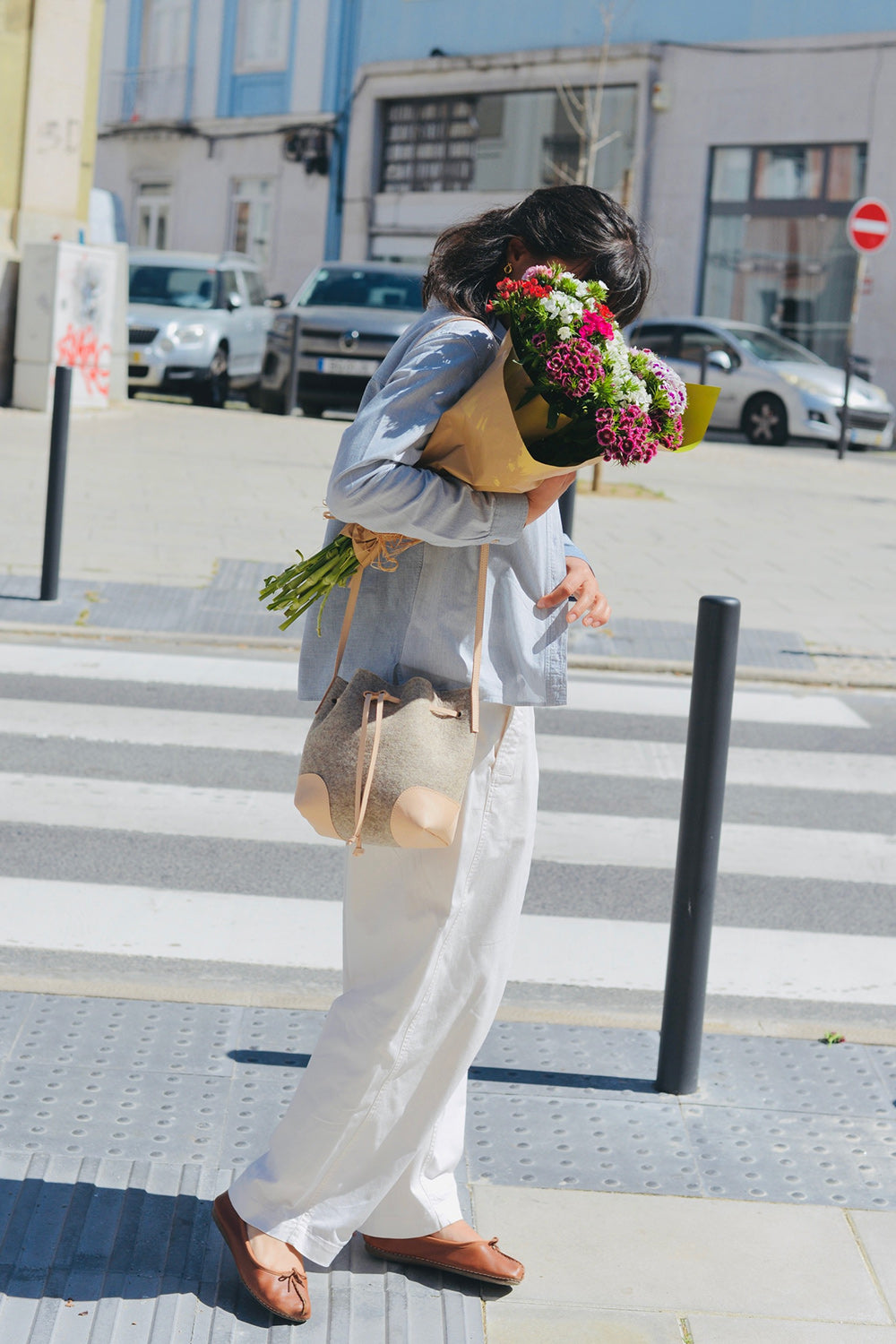 Person holding flowers and a wool felt bucket bag on a city street
