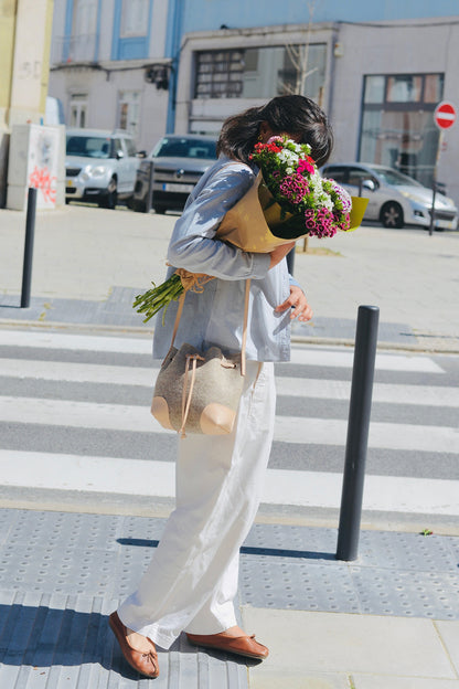 Person holding flowers and a wool felt bucket bag on a city street