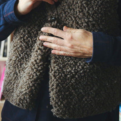Samarra vest. Close-up of a hand adjusting a brown knitted wool garment.
