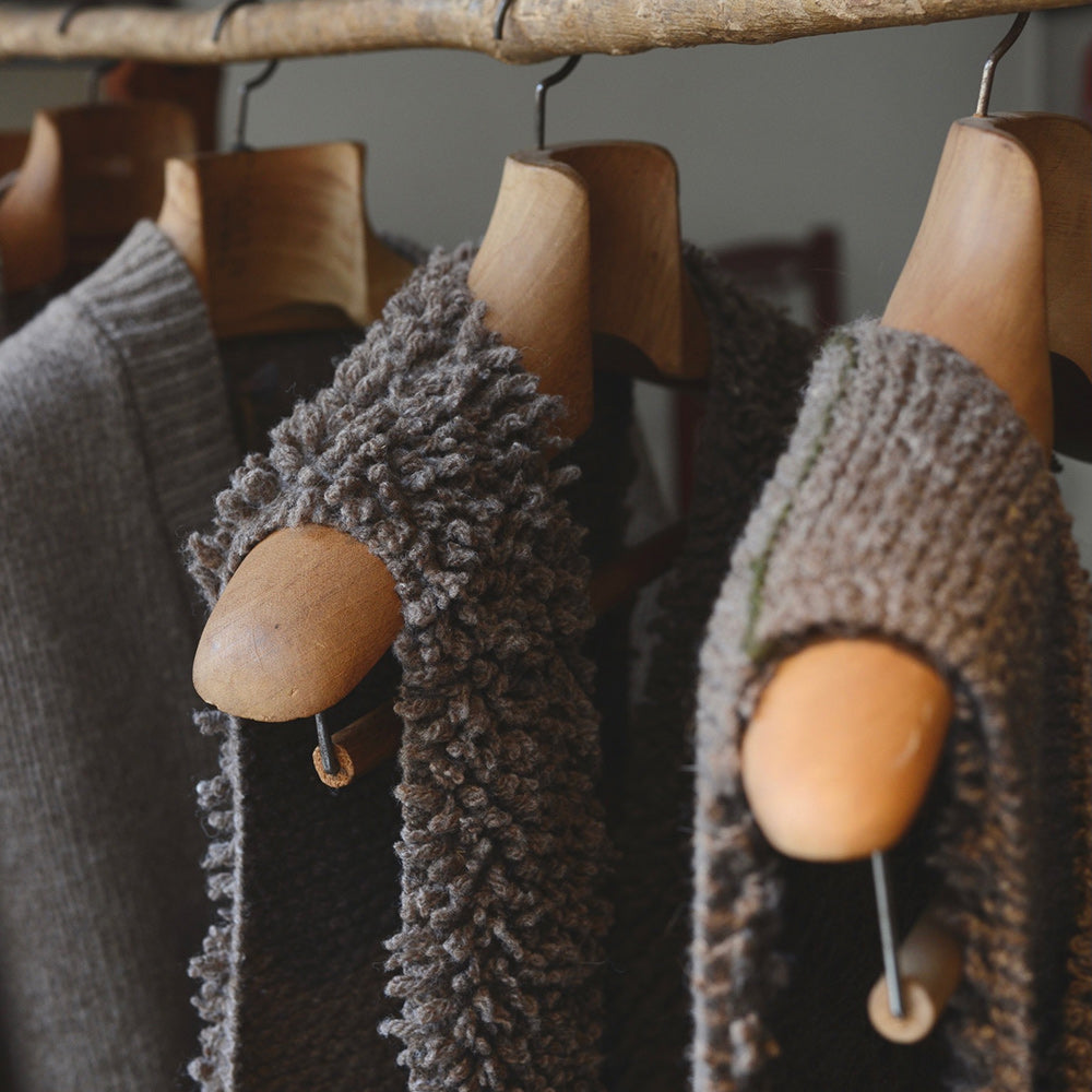 Samarra vest. Knitted sweaters hanging on wooden hangers against a neutral background