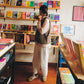 Person wearing a knitted wool vest and browsing books in a bookstore with shelves filled with colorful books.