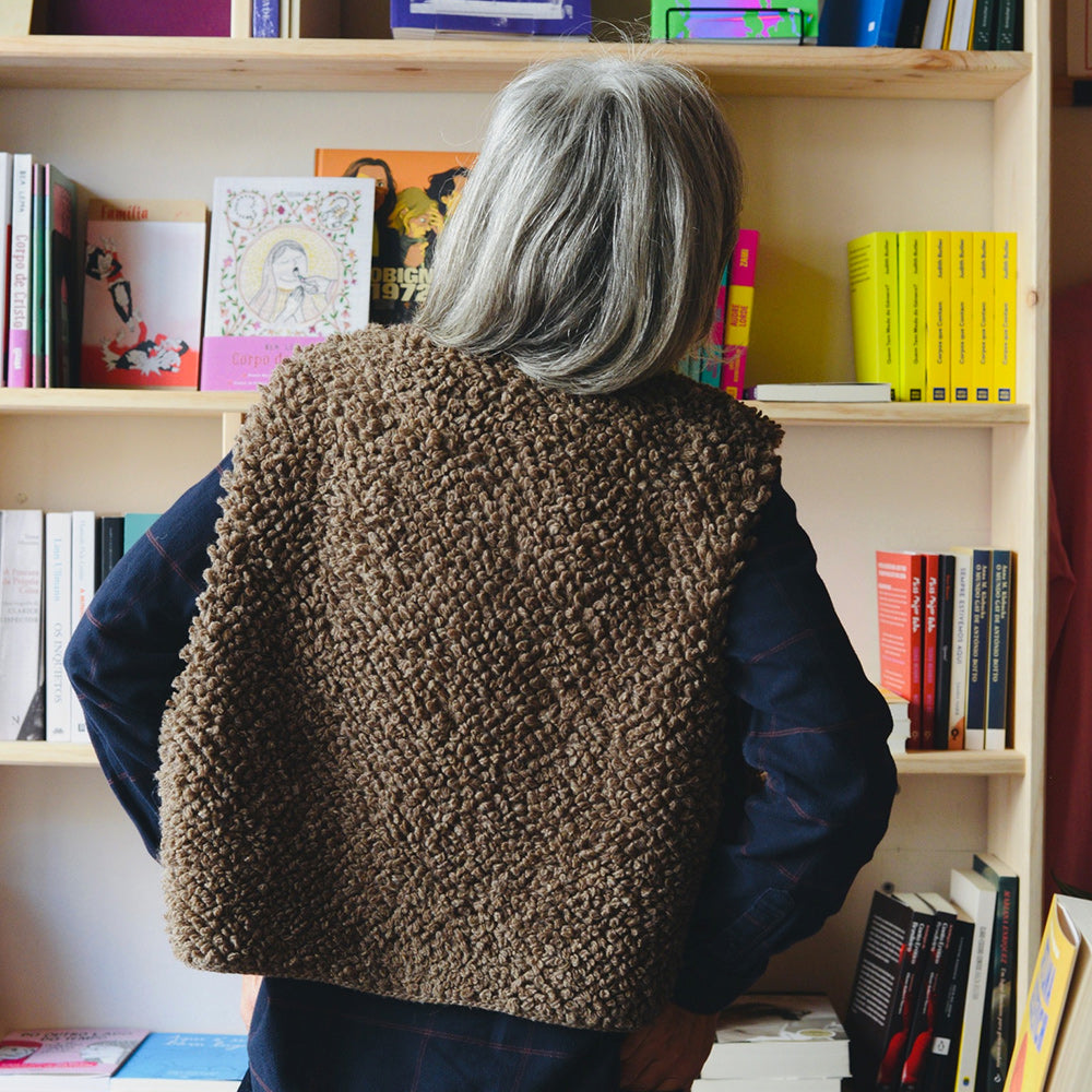 Person wearing a brown textured sweater standing in front of a bookshelf filled with books.