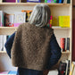 Person wearing a brown textured sweater standing in front of a bookshelf filled with books.