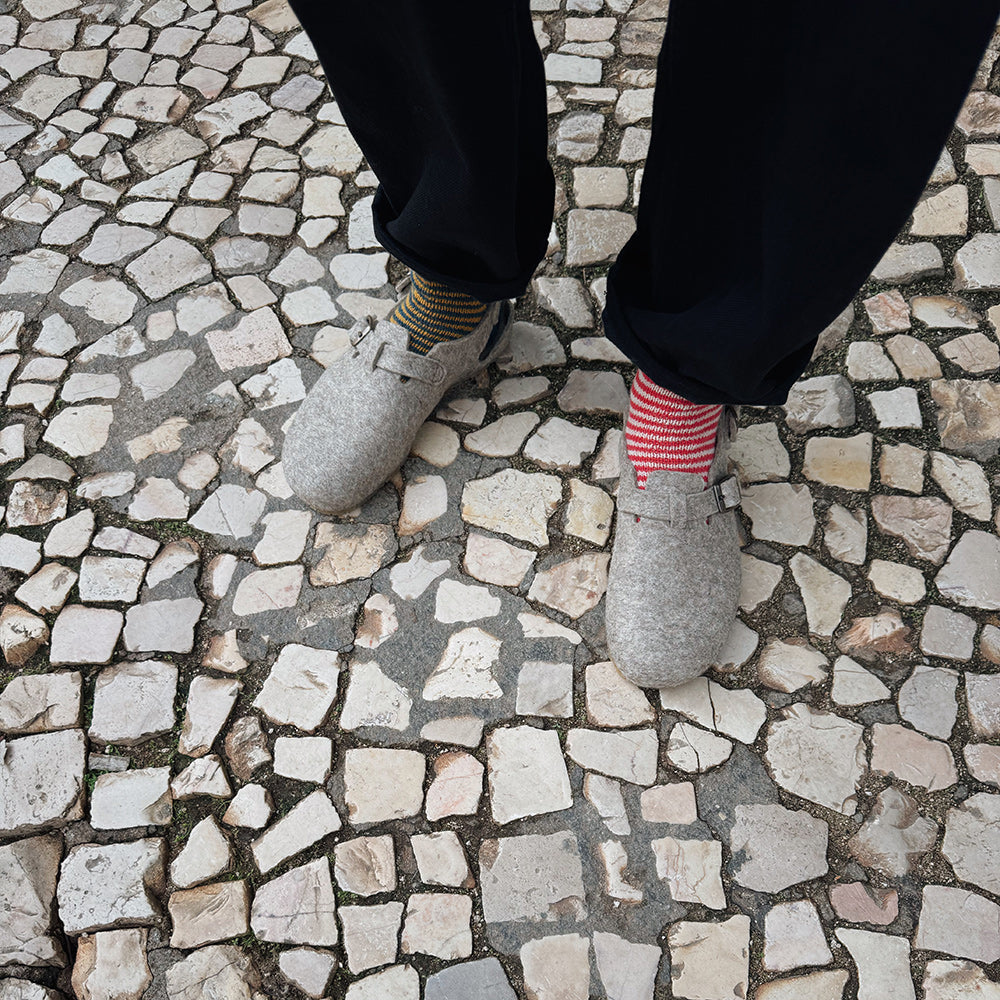 Person wearing wool felt clogs / sandals and colorful handknit socks on a stone pavement in Lisbon